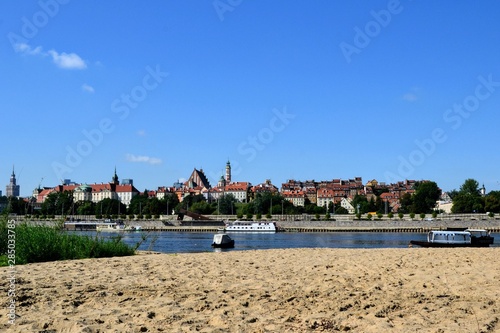 Warsaw, Poland. Scenic view of the Old Town - historic quarter of Warsaw with Royal Castle and red roof tenements seen from the sandy beach located on the wild Vistula river side. 