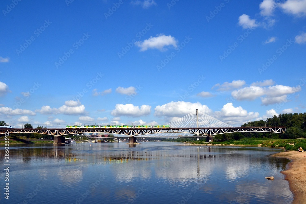 The green /yellow train running through the Srednicowy railway bridge in Warsaw, Poland. View from the Stadium Beach (or Poniatowka beach) in the vicinity of the National Stadium. 