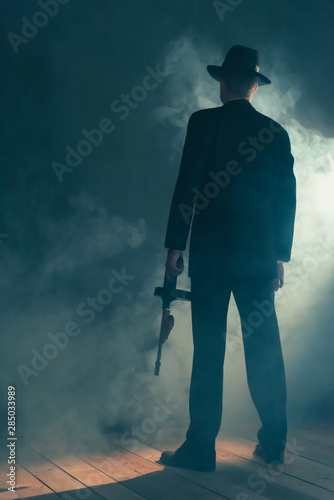 Retro gangster stands with machine gun in smoky room. Rear view. © ysbrandcosijn