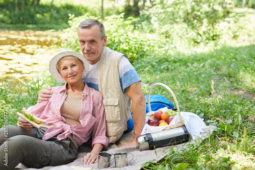 Portrait of mature couple sitting on the grass and looking at camera they have a picnic in nature © AnnaStills
