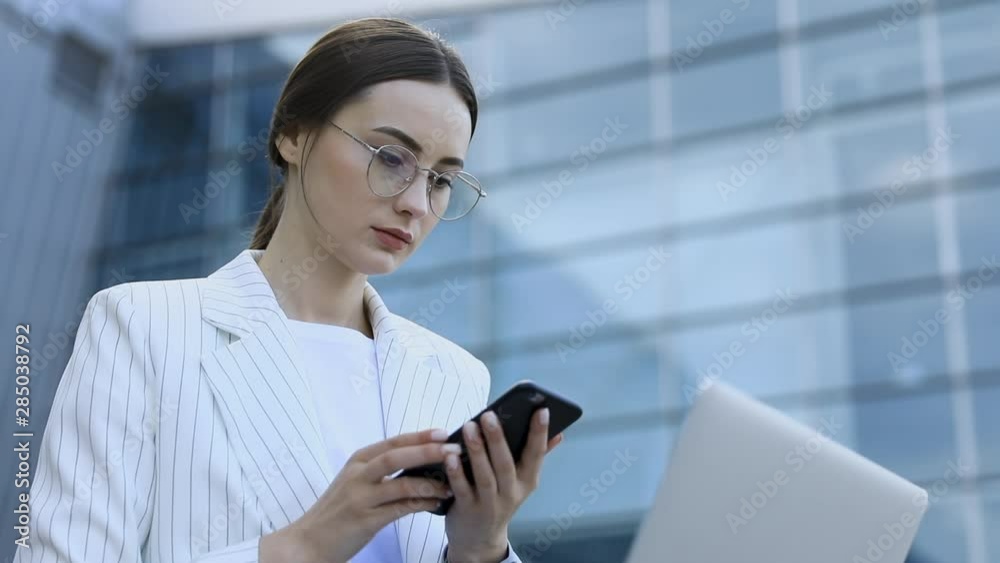 Close-up of young professional businesswoman using her laptop outside while working at modern business center, modern buildings in the background, flare light, film effects, slow motion Close-up of young professional businesswoman using her laptop outside while working at modern business center, modern buildings in the background, flare light, film effects, slow motion