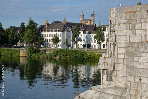 Close-up on the carvings of the 13th century roman bridge Sint Servaasbrug, with historic buildings on the Meuse river Western banks (basilica of our Lady) in the background, Maastricht, Netherlands photo