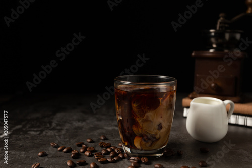 Milk pouring into iced black coffee on table and black background.