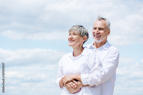 happy senior couple in white shirts embracing under blue sky © LIGHTFIELD STUDIOS