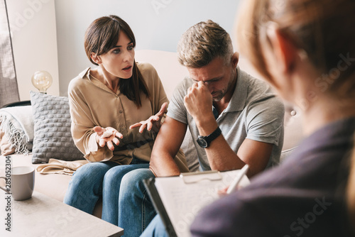 Photo of puzzled annoyed couple having conversation with psychologist on therapy session in room