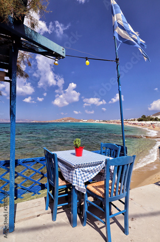 Single blue dining table and chairs with Greek flag overlooking turquoise clear Aegean Sea and beach at Agios Prokopios, Naxos, Greek Islands photo