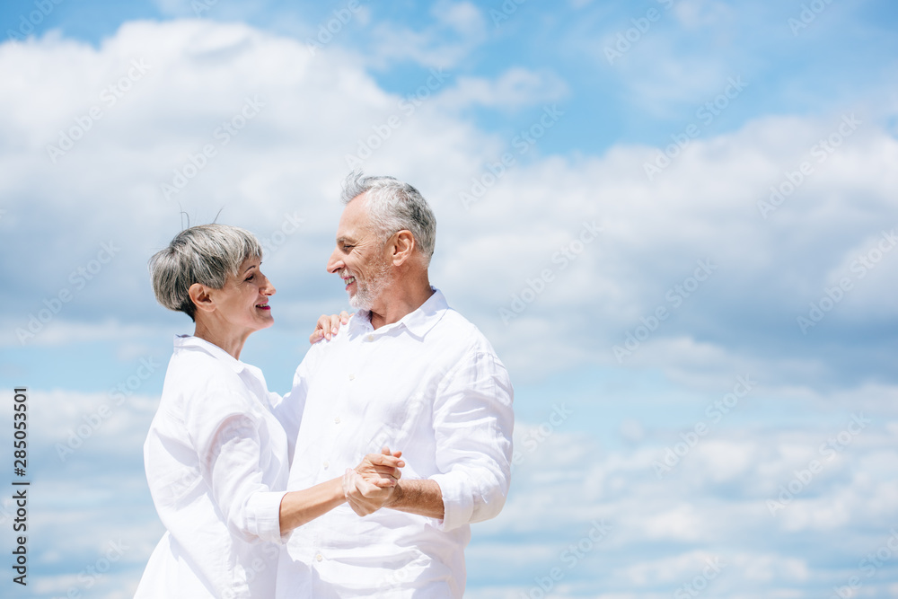 happy senior couple looking at each other while dancing under blue sky happy senior couple looking at each other while dancing under blue sky