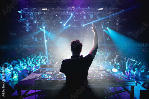 Fotografie, Obraz Silhouette of DJ in nightclub with hands up, shot from behind