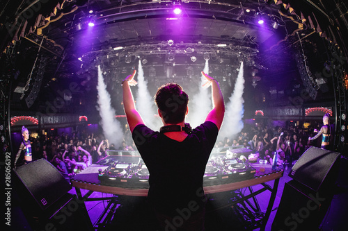 Fototapeta DJ in nightclub with hands up and cryo canons, shot from behind
