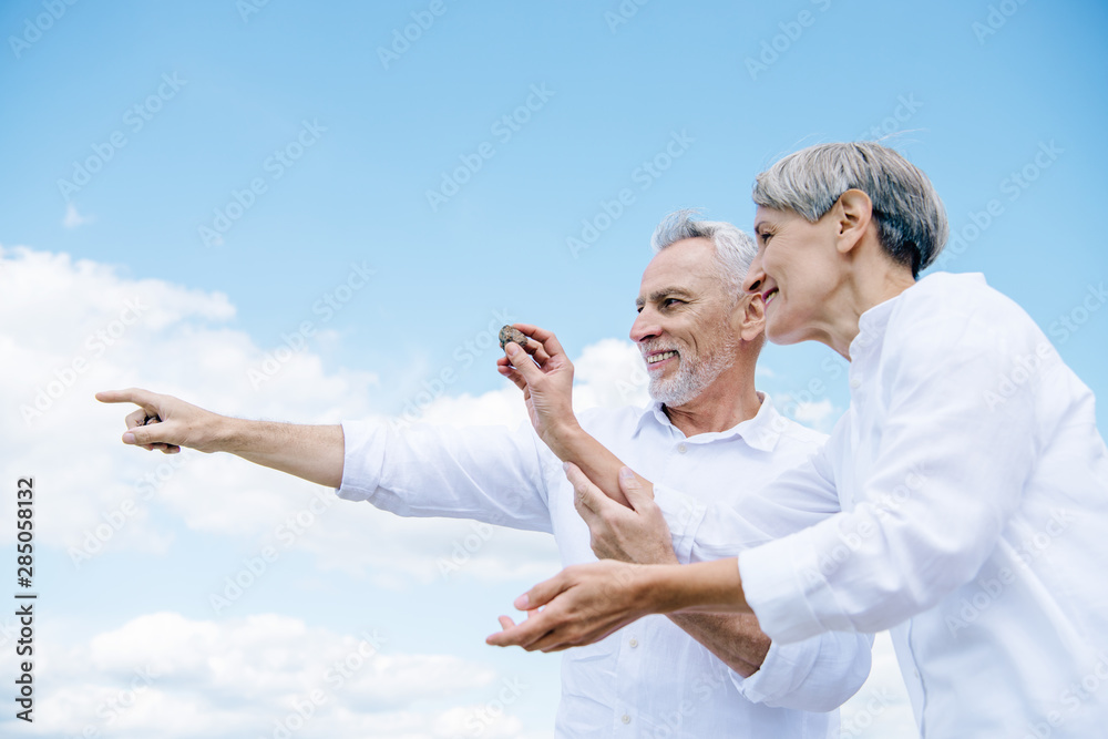 happy smiling senior couple holding stone and pointing with finger under blue sky happy smiling senior couple holding stone and pointing with finger under blue sky