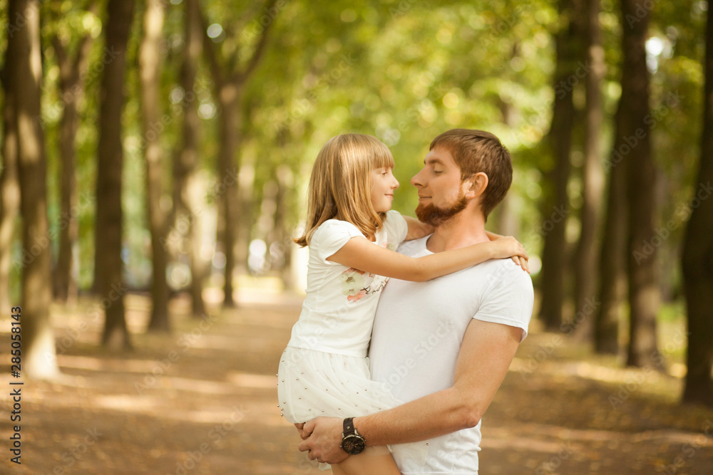 Fototapeta premium Portrait of lovely smiling daughter in her father's arms walking at green park outside. Happy family people concept