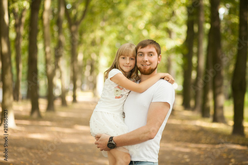 Portrait of lovely smiling daughter in her father's arms walking at green park outside. Happy family people concept