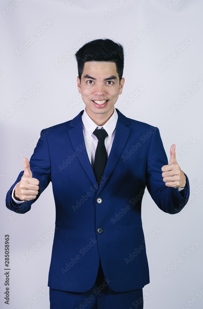 Portrait handsome young asian .businessman wearing a blue suit showing thumbs up sign isolated on grey background in studio. Asian man people. business success concept. Portrait handsome young asian .businessman wearing a blue suit showing thumbs up sign isolated on grey background in studio. Asian man people. business success concept.