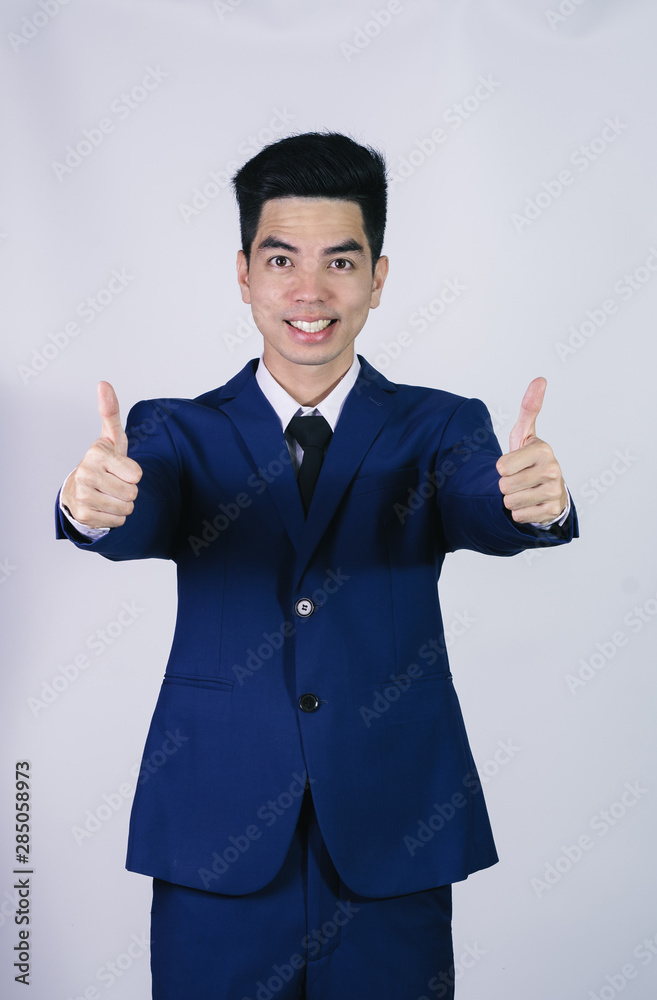 Portrait handsome young asian .businessman wearing a blue suit showing thumbs up sign isolated on grey background in studio. Asian man people. business success concept. Portrait handsome young asian .businessman wearing a blue suit showing thumbs up sign isolated on grey background in studio. Asian man people. business success concept.