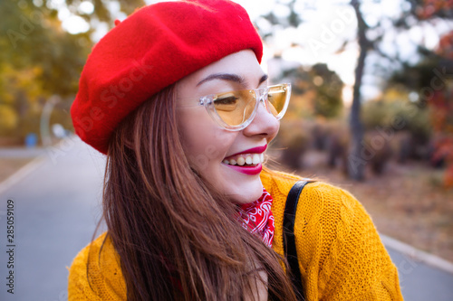 Fashion happy young woman in knitted hat and sweater having fun outside in the autumn park.Beautiful young woman in yellow sweater and nice trendy hat looking thoughtful in autumn park. 