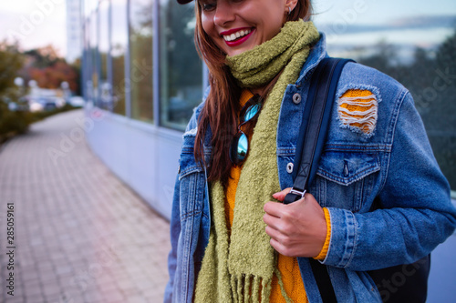 Fashionable young woman in jeans, long jeans jackeт, orange hoodie and handbag on the city streets. Fashion.Stylish.Close up image of fashion details, jeans jacket, stylish bag.