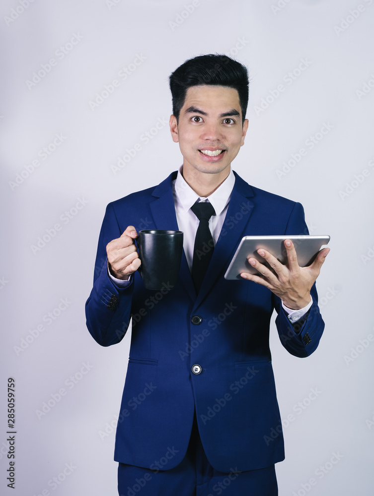 Portrait handsome young asian man wearing a blue suit holding smart phone or tablet smile and happy isolated on gray background in studio. Asian man people. business success concept. Portrait handsome young asian man wearing a blue suit holding smart phone or tablet smile and happy isolated on gray background in studio. Asian man people. business success concept.