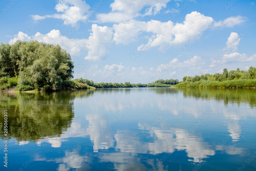 Blue beautiful sky against the background of the river. Clouds are displayed in calm water. On the horizon, the green bank of the Dniester, place for fishing
