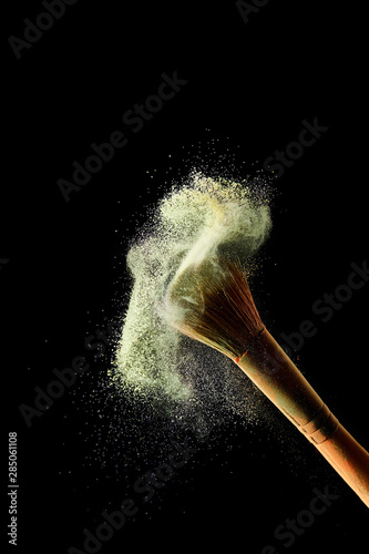 cosmetic brush with colorful powder explosion on black background