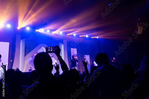 Silhouettes of people show with hands in the air in a bright in the pop rock concert in front of the stage. Hands with gesture Horns. rocks Party in a club.