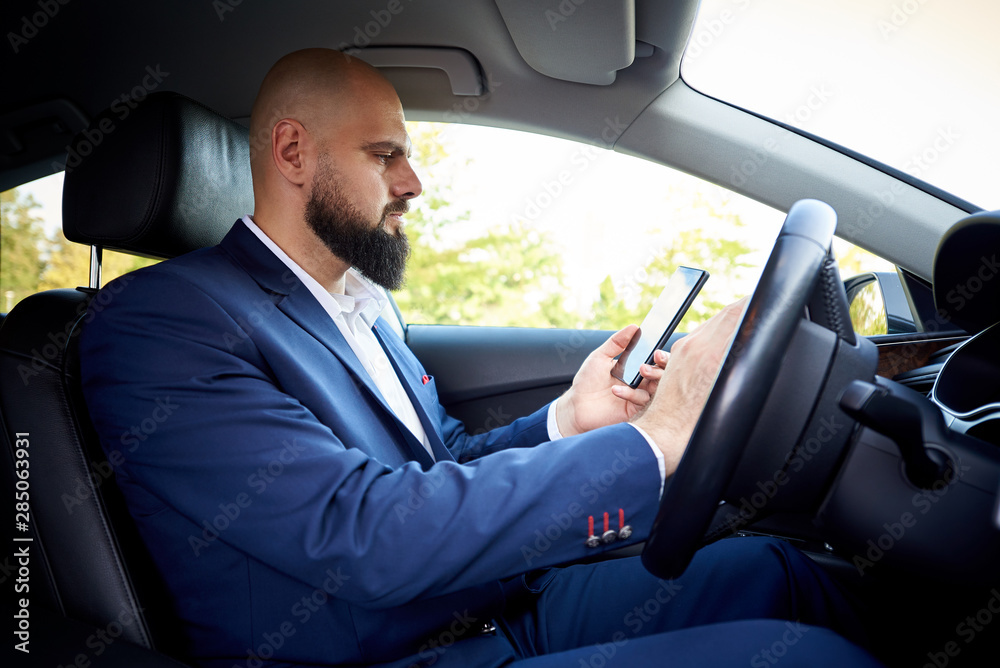 Successful young man with a smartphone in the car.