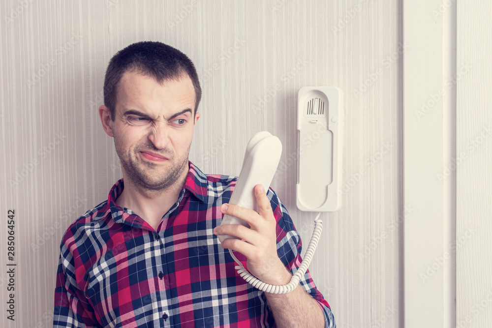Guy with intercom or phone land line, man has an unpleasant conversation, guy does not want to listen to the interlocutor, portrait, toned