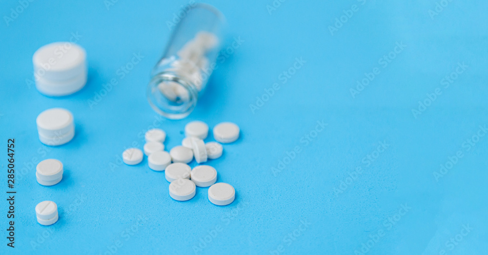 White pills and glass bottle on blue background. Alternative homeopathy is a herb medicine.The concept of health and medicine. Flatley. The view from the top. copyspace for text. White pills and glass bottle on blue background. Alternative homeopathy is a herb medicine.The concept of health and medicine. Flatley. The view from the top. copyspace for text.