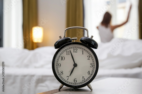 Young beautiful woman waking up and stretching at seven o clock in the morning, a good start of the day