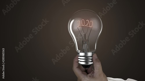 Hand holding lighting bulb lamp with 2020 on black dark background, 3D rendering animation, macro view