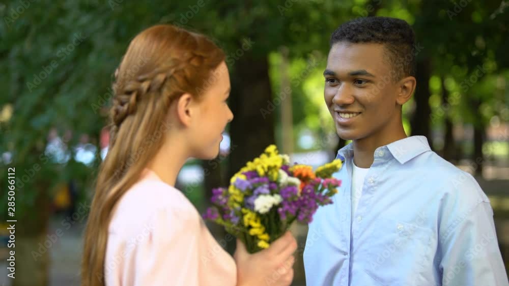 Sweet Afro-American teen boy presenting bunch of flowers to shy girlfriend Sweet Afro-American teen boy presenting bunch of flowers to shy girlfriend