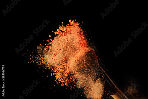 cosmetic brush with colorful orange powder explosion on black background
