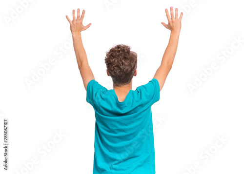 Back view of teen boy holding hands up and celebrating success. Cheerful teenager in blue T-shirt celebrating something - rear view. Happy child isolated on white background.