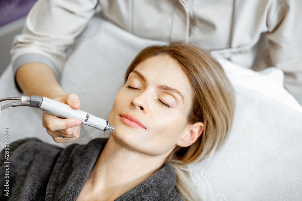 Cosmetologist making vacuum hydro peeling on the cheek area to a woman at the luxury beauty salon. Concept of a professional facial treatment Cosmetologist making vacuum hydro peeling on the cheek area to a woman at the luxury beauty salon. Concept of a professional facial treatment