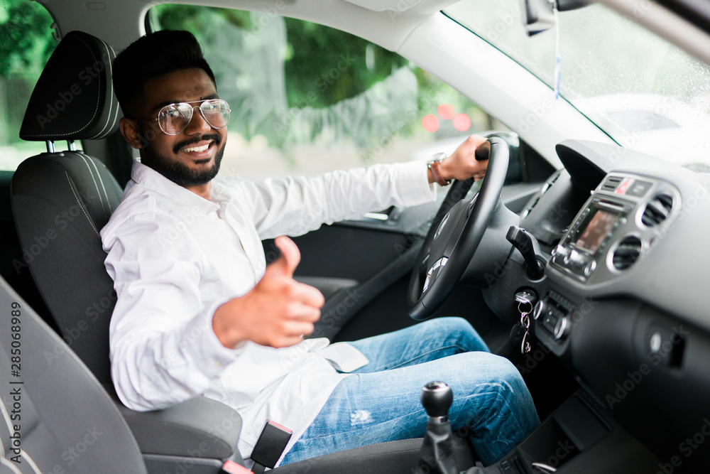 Young indian man smiling and showing thumb up in his car.
