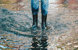 Legs of woman in shabby jeans with black rubber boots standing in a puddle of water after rain.