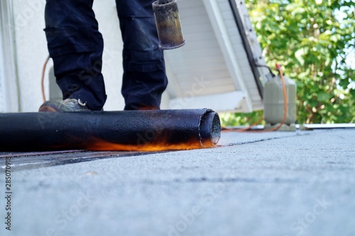 Flat roof installation with propane blowtorch during construction works with roofing felt. Heating and melting bitumen roofing felt. Roofing felt. Roofer working. Roofer working tool. Waterproofing