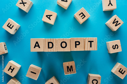 top view of adopt word made of wooden blocks on blue background