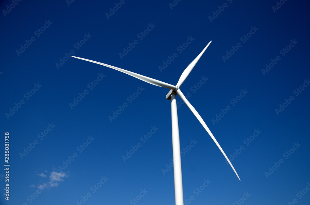 Against a clear blue sky, three blades of a wind farm Against a clear blue sky, three blades of a wind farm