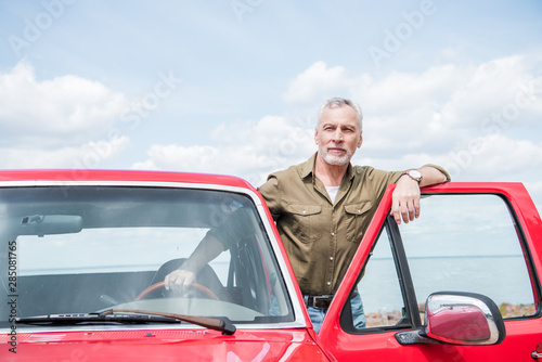 senior man in shirt in red car in sunny day