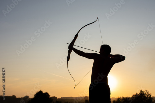 Valokuva Silhouette of a man with an ancient weapon bow and arrow on a background of sky
