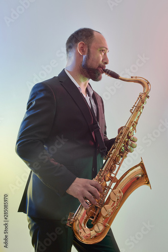 Portrait of professional musician saxophonist man in suit plays jazz music on saxophone, white background in a photo studio, side view