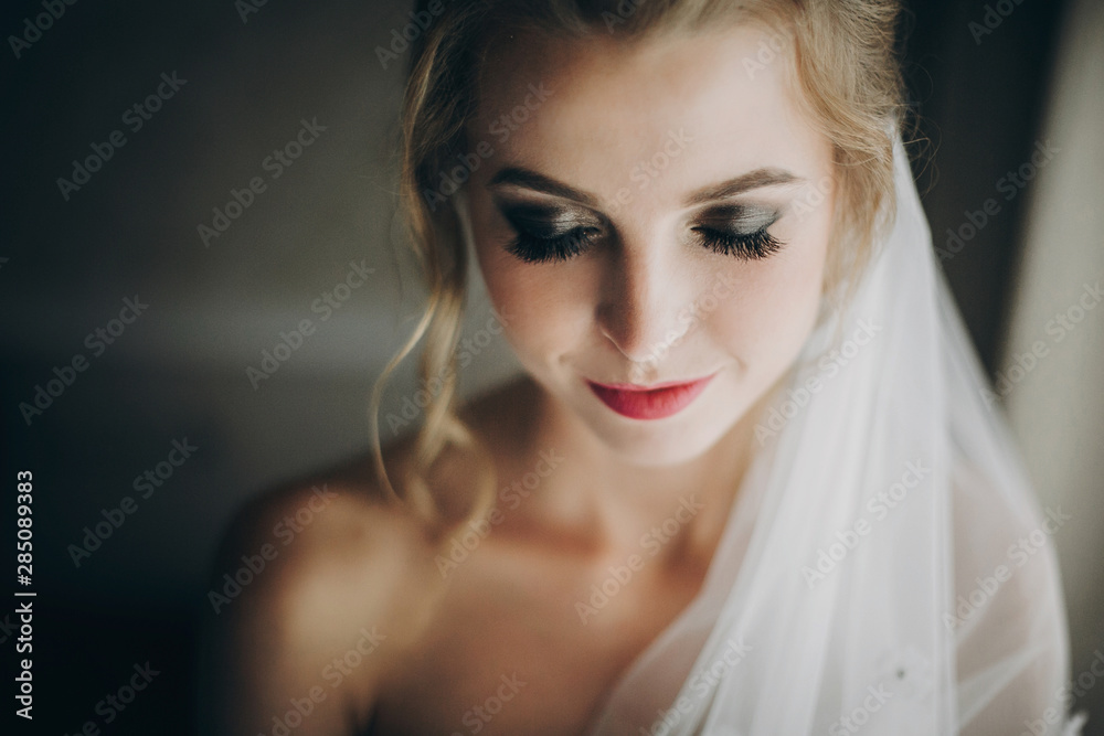 Stylish happy bride smiling and posing in soft light near window in hotel room. Morning preparation before wedding ceremony. Gorgeous bride portrait Stylish happy bride smiling and posing in soft light near window in hotel room. Morning preparation before wedding ceremony. Gorgeous bride portrait