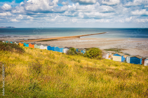 A sandbank creates a spit of land that is only accessible at low tide in Whitstable, Kent, UK. A beautiful landscape including beach huts a cloudscape and a sloping verge full of wild grass. photo