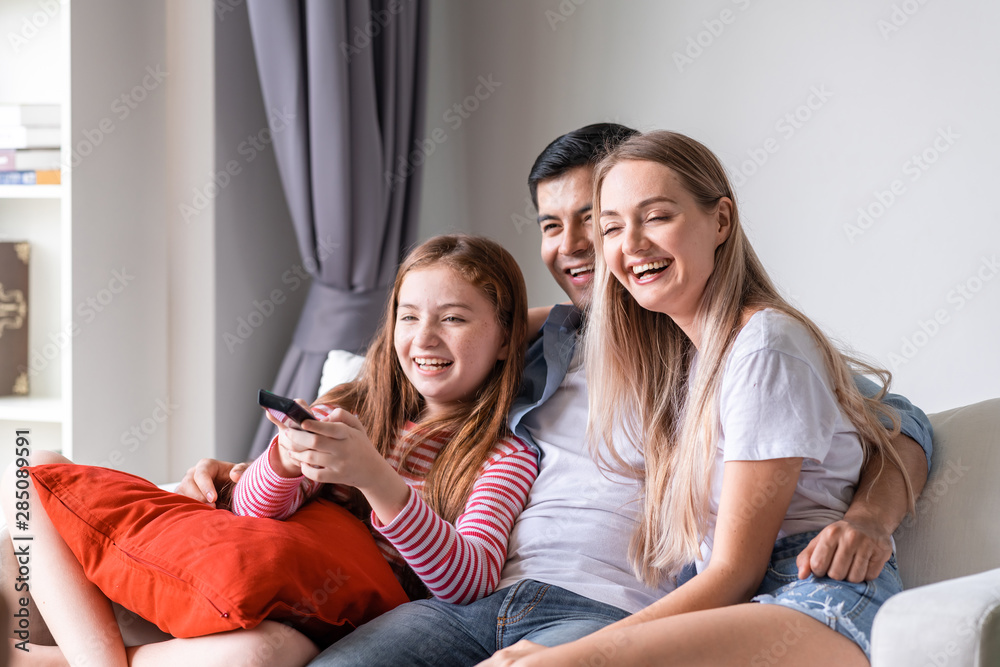 Happy family watching tv on couch in living room at home. White man, woman, girl. Happy laughing. Happy family watching tv on couch in living room at home. White man, woman, girl. Happy laughing.
