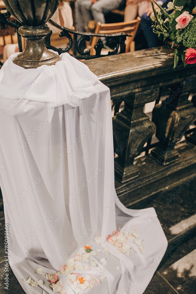 Stylish wedding decor of wooden benches in church for holy matrimony. Beautiful roses and tulle bouquets on wooden chairs, arrangement of aisle in church