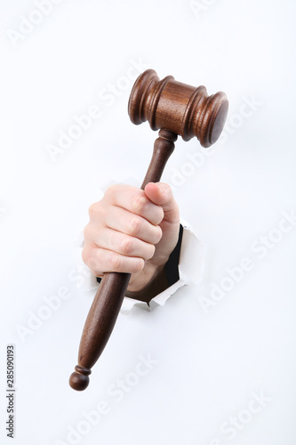 Hand holding judge gavel from white torn paper