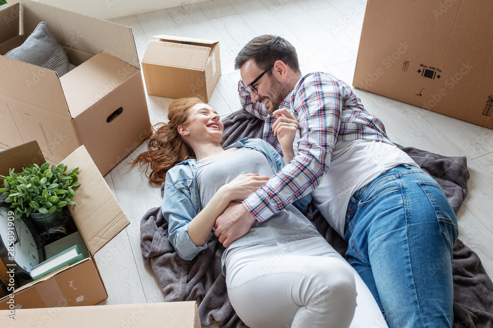 Young couple lying at the floor in empty room with unpacked boxes all arround Young couple lying at the floor in empty room with unpacked boxes all arround