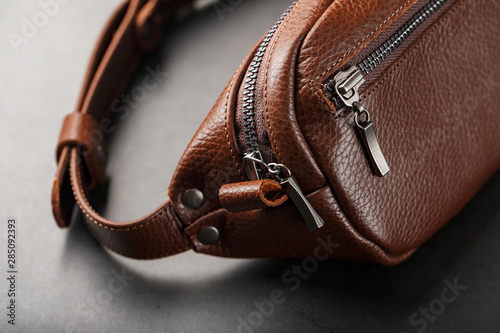 A brown belt bag made of textured brown leather on a black stone background. Elegant fanny pack brown bag with a zipper