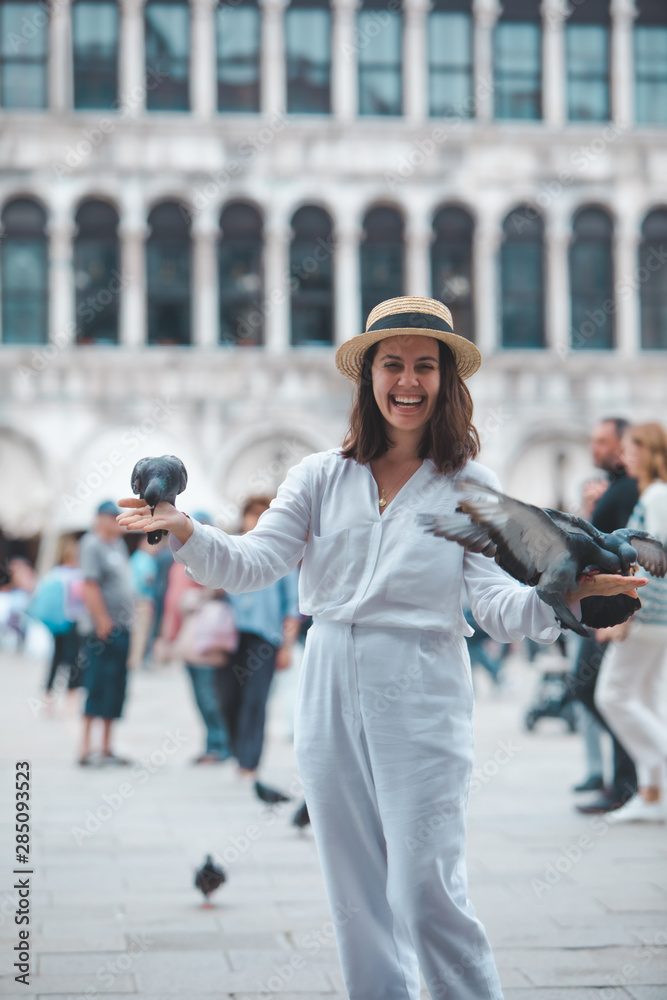 woman in white clothes with straw hat having fun with pigeons at venice city square