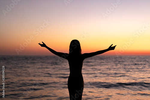 Silhouette of beautiful young gracile pensive woman with a freedom feeling  rise hand up on beautiful sunset. Freedom and travel adventure happy feeling concept. © Juliaap